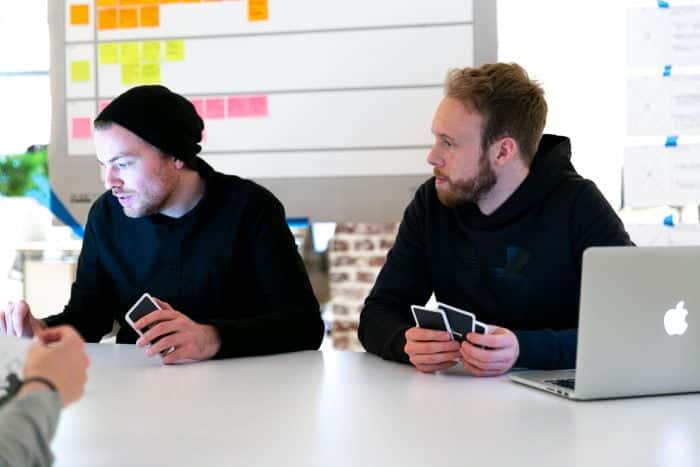 Zwei Mitarbeiter von Me & Company mit Planning Poker Karten vor Laptops