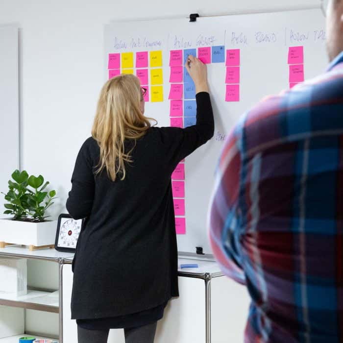 Mitarbeiterin von Me & Company arbeitet mit Post-its am Whiteboard im Rahmen ihrer Rolle als Growth Hacker