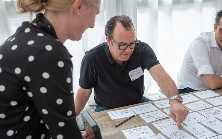Trainingsteilnehmer unterhält sich mit Trainerin und zeigt dabei auf die vor sich liegenden Arbeitsergebnisse
