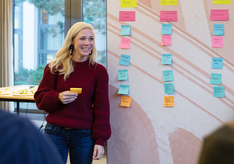 Eine gut gelaunte Teilnehmerin des Workshops steht vor einer Wand, die mit Post-its gefüllt ist