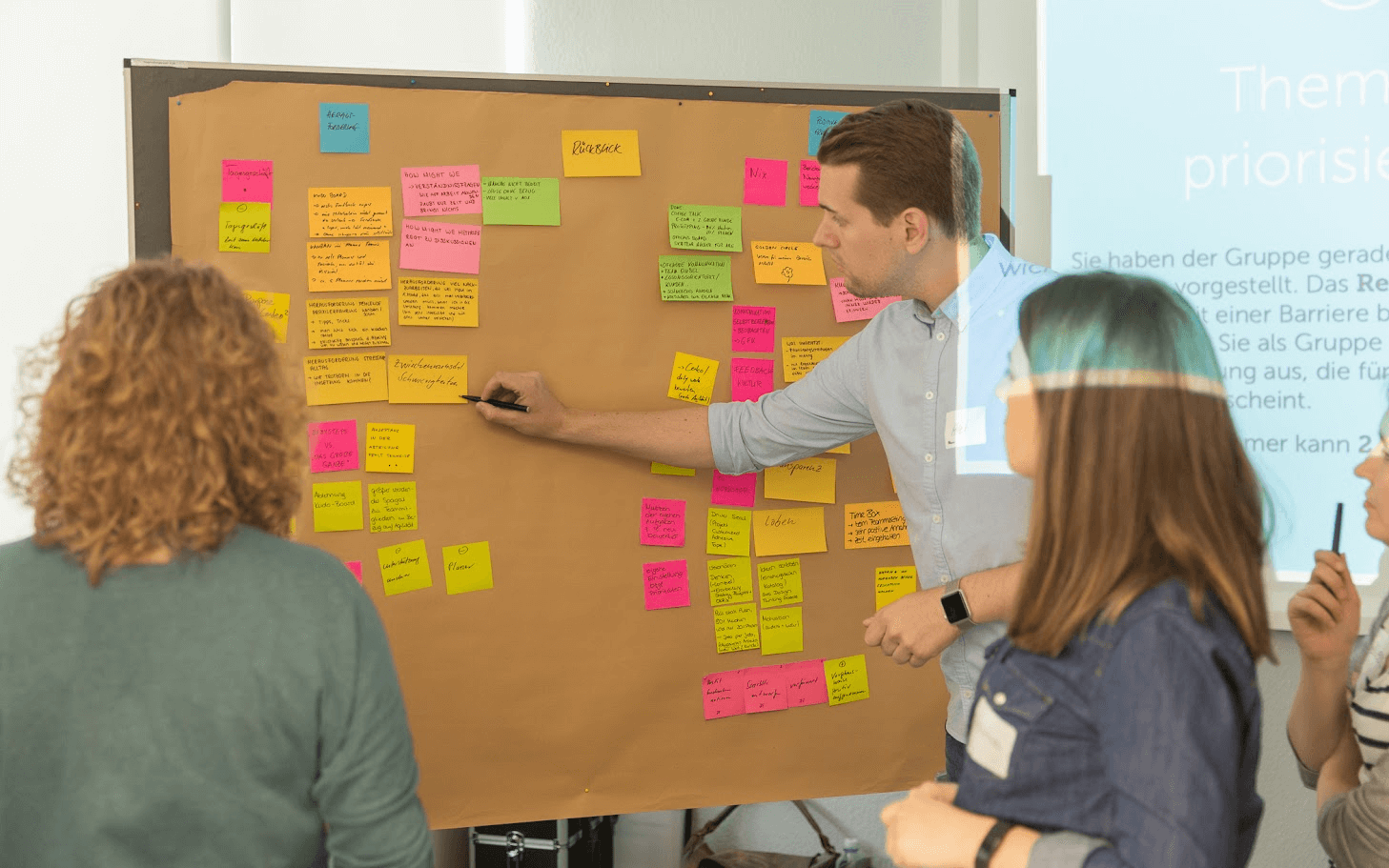 Ein Mann zeigt etwas auf einer Pinnwand mit aufgeklebten Post-Its