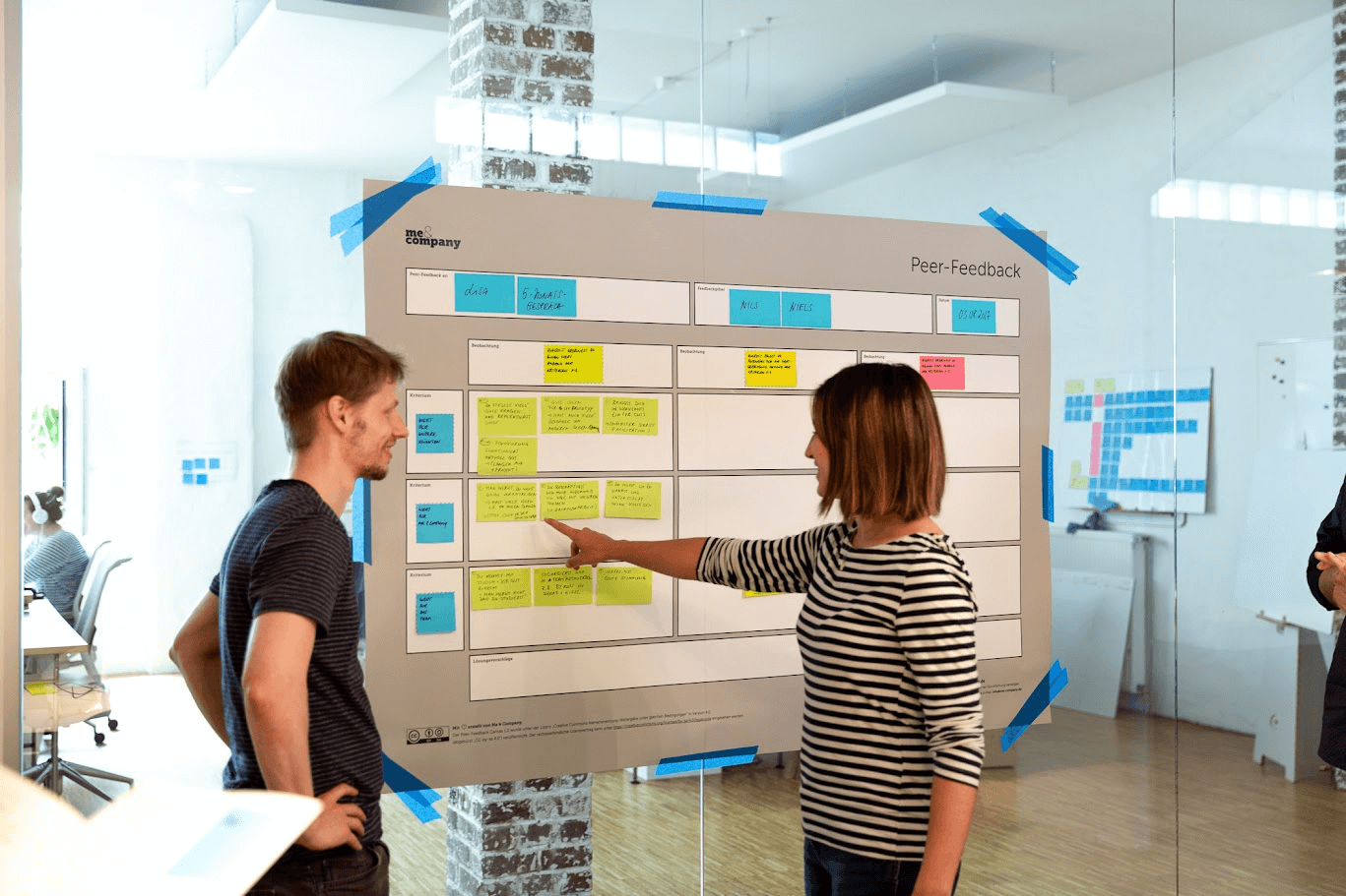 Zwei Personen stehen vor einem Plakat zum Thema Peer Feedbacks