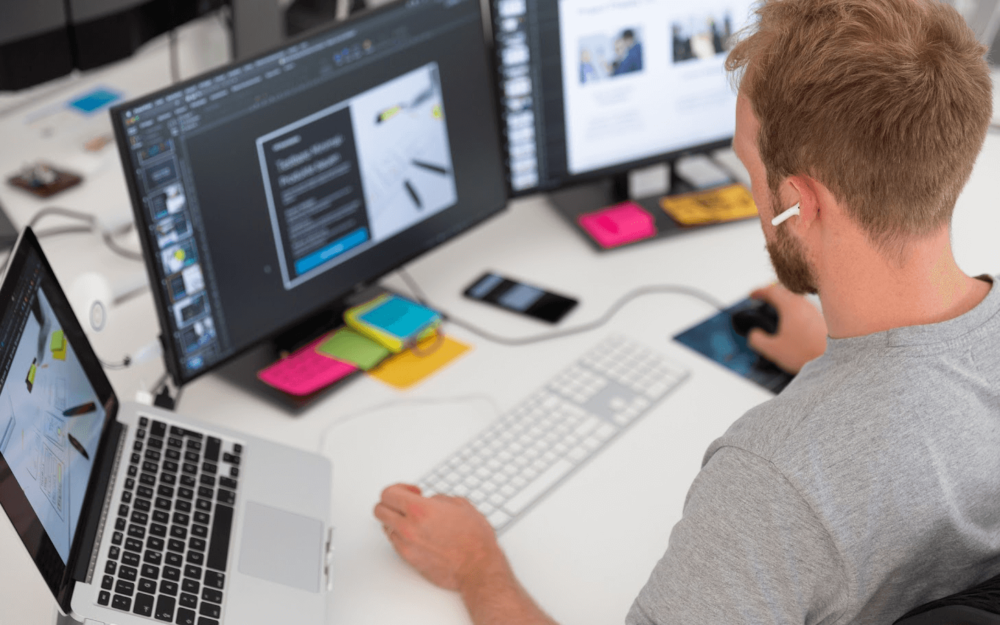 Eine Person arbeitet an einem Schreibtisch mit Laptop und zwei Monitoren.